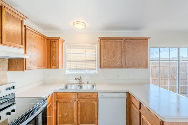 Kitchen with dishwasher, stainless steel electric range oven, under cabinet range hood, ornamental molding, and light countertops | Image 9
