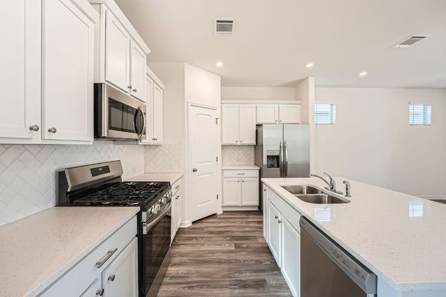 Kitchen featuring dark wood-style floors, visible vents, an island with sink, a sink, and appliances with stainless steel finishes | Image 10