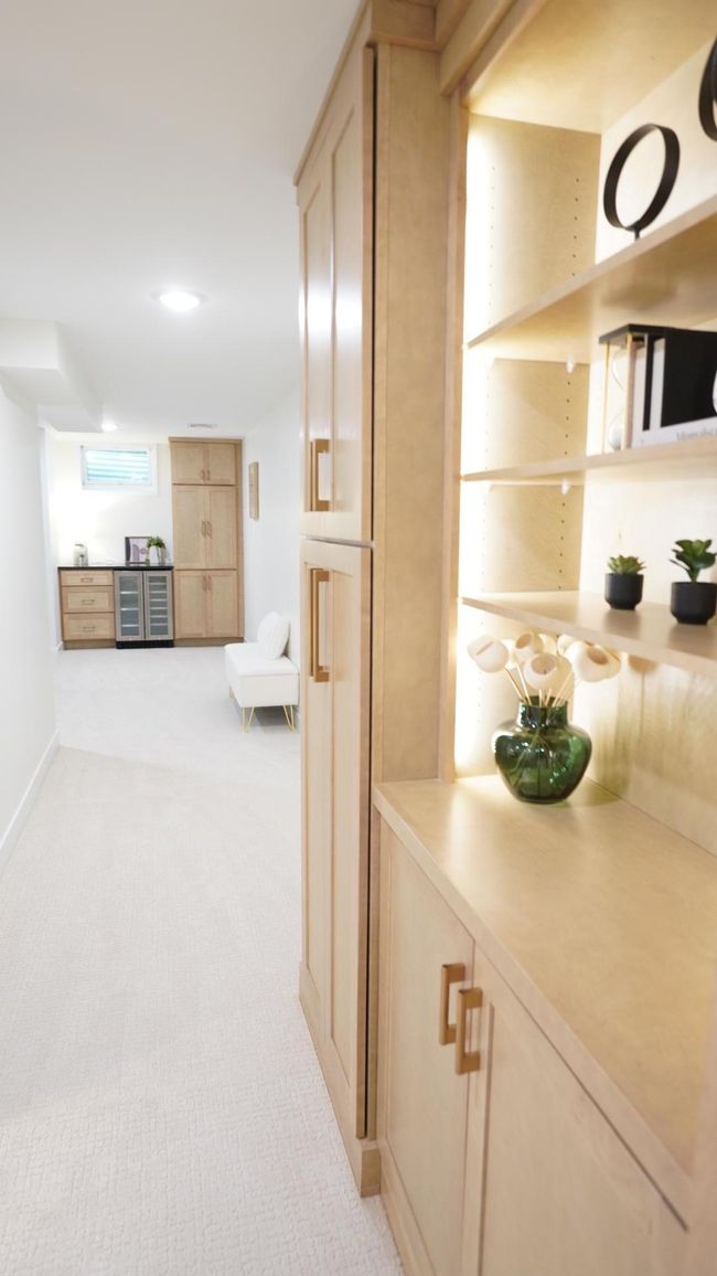 Custom cabinets abound throughout this home, including the gorgeously stained birch cabinets of both the large storage built-in and the dry bar down the hall. The light gold hardware adds a touch of elegance in this warm and inviting basement space. | Image 18