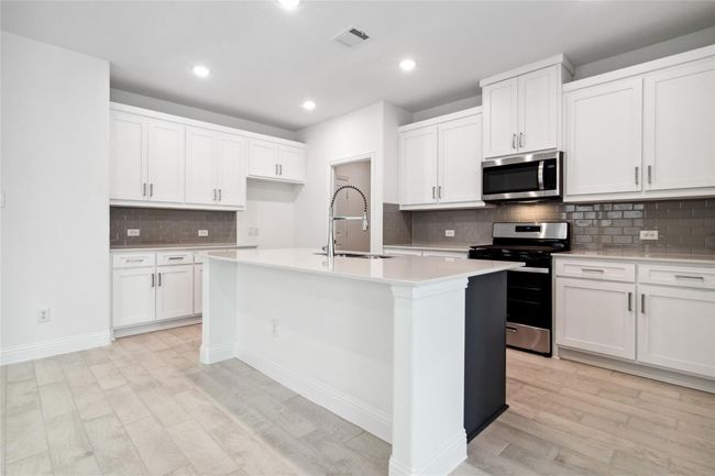 Kitchen with appliances with stainless steel finishes, white cabinets, decorative backsplash, light wood-style floors, and recessed lighting | Image 25