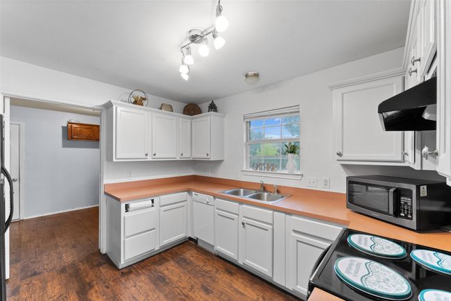 Kitchen featuring stainless steel microwave, extractor fan, light countertops, and white cabinetry | Image 11