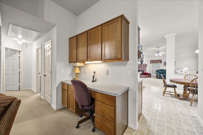 Home office featuring attic access, a ceiling fan, built in study area, light colored carpet, and a fireplace | Image 23