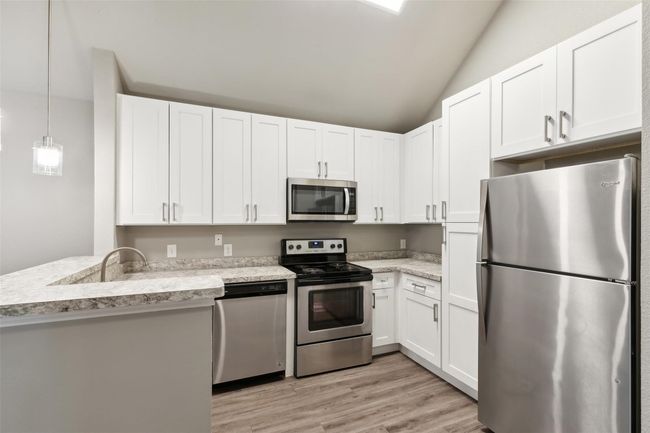 Kitchen featuring stainless steel appliances, white cabinets, light wood-style flooring, vaulted ceiling, and a peninsula | Image 4