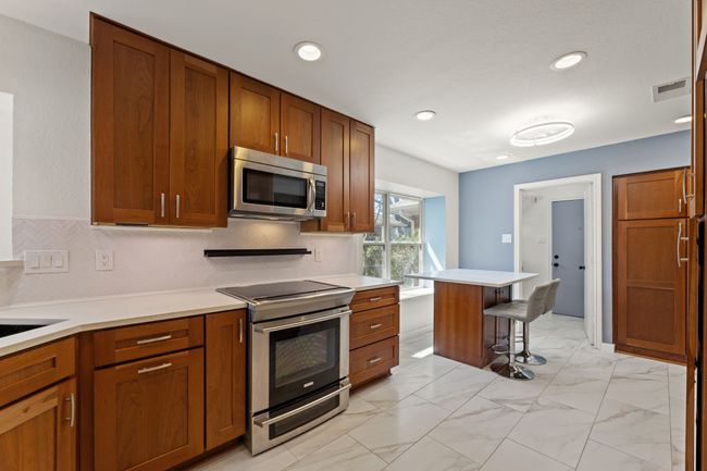 Kitchen featuring light countertops, a breakfast bar area, stainless steel appliances, marble finish floor, and brown cabinetry | Image 7