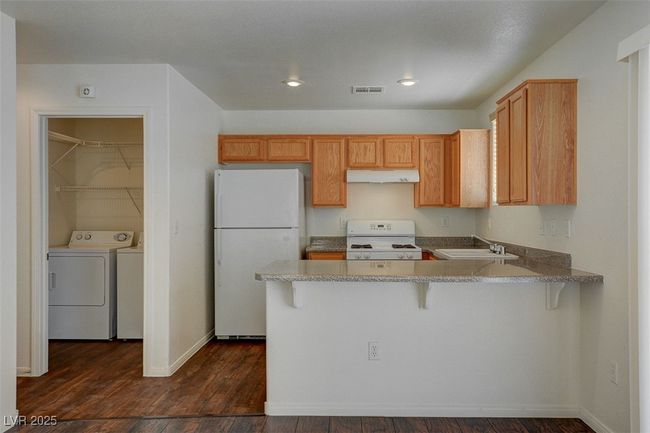 Kitchen featuring white appliances, independent washer and dryer, under cabinet range hood, a sink, and visible vents | Image 8