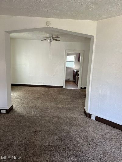 Empty room featuring a textured ceiling, carpet flooring, ceiling fan, and a baseboard heating unit | Image 3