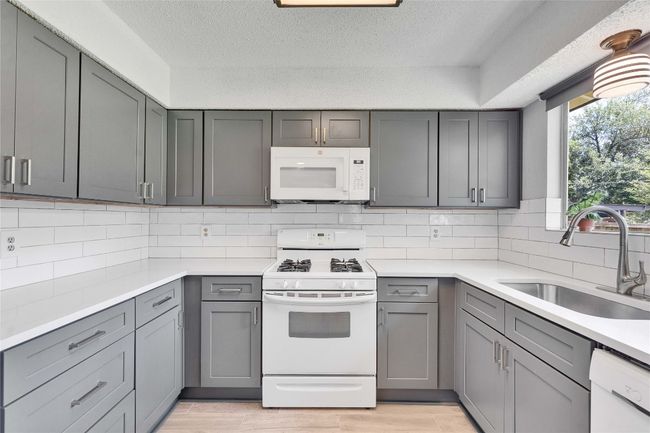 Kitchen with white appliances, gray cabinetry, light countertops, tasteful backsplash, and a textured ceiling | Image 11