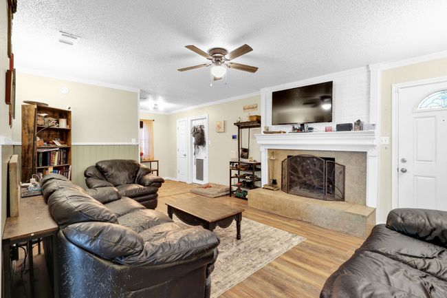 Living room featuring wood finished floors, a ceiling fan, a fireplace, ornamental molding, and a textured ceiling | Image 16