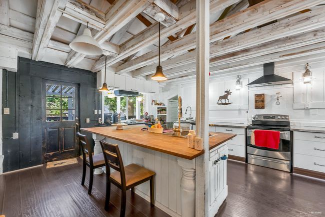 Kitchen with stainless steel electric range oven, wall chimney exhaust hood, white cabinetry, and butcher block countertops | Image 9