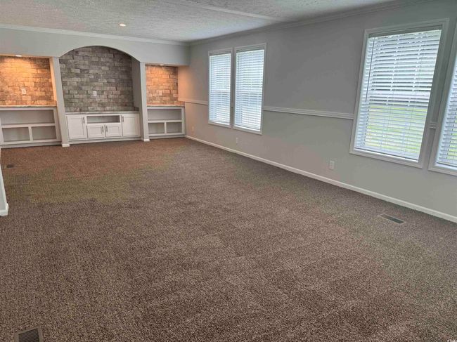 Unfurnished living room featuring a textured ceiling, crown molding, healthy amount of natural light, and dark colored carpet | Image 32