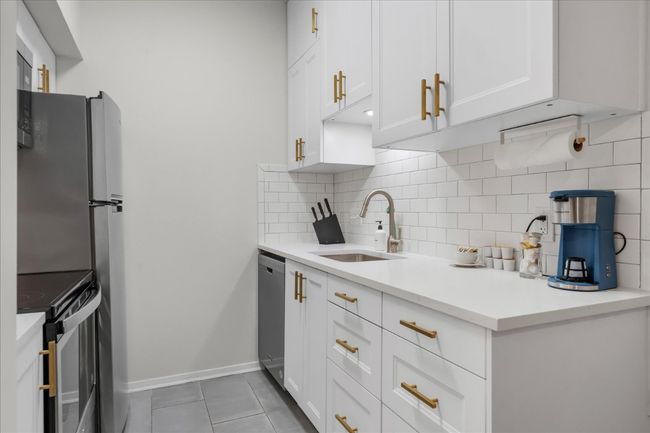 Kitchen featuring appliances with stainless steel finishes, tasteful backsplash, white cabinets, light tile patterned flooring, and light countertops | Image 13