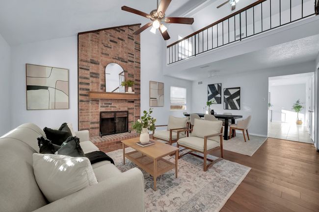 Living area featuring a ceiling fan, a brick fireplace, wood-type flooring, and high vaulted ceiling | Image 5