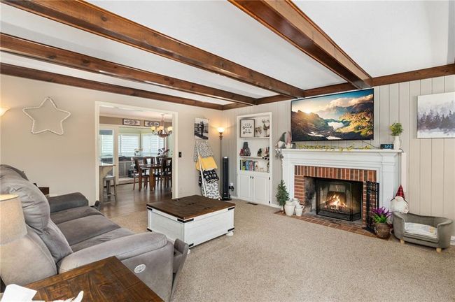 Carpeted living room with an inviting chandelier, beam ceiling, and a brick fireplace | Image 21