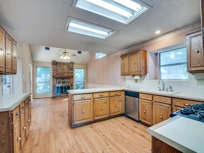 Kitchen featuring dishwasher, a peninsula, light wood-style flooring, a fireplace, and a textured ceiling | Image 7