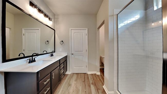 Full bath featuring wood finished floors, double vanity, a stall shower, toilet, and baseboards | Image 6