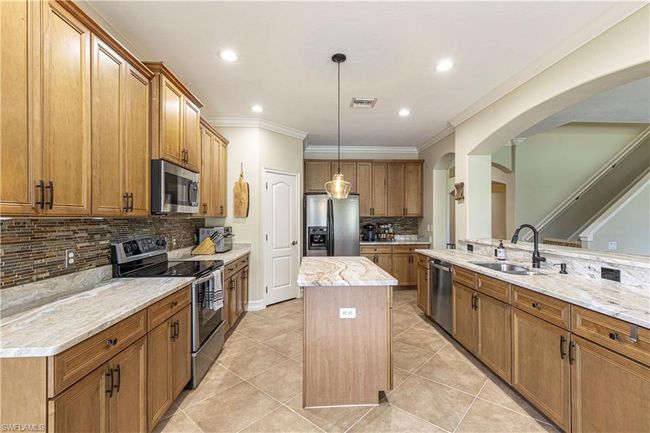 Kitchen with a center island, brown cabinetry, light tile patterned flooring, arched walkways, and stainless steel appliances | Image 10