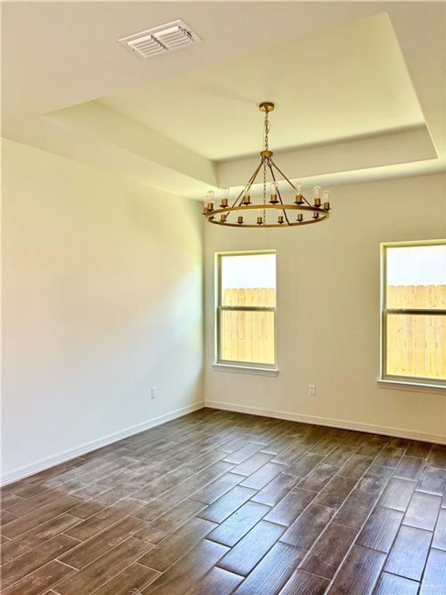 Empty room featuring dark wood finished floors, visible vents, a notable chandelier, and a raised ceiling | Image 4