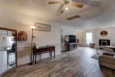 Living room featuring wood look tile floors, ceiling fan, a textured ceiling, and a large fireplace | Image 3