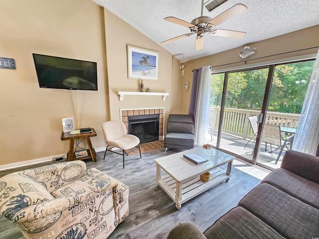 Living room featuring a textured ceiling, vaulted ceiling, a tile fireplace, a ceiling fan, and wood finished floors | Image 10