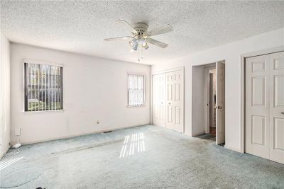 Unfurnished bedroom with ceiling fan, multiple closets, a textured ceiling, and light colored carpet | Image 3