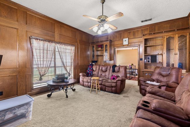 Living area featuring crown molding, a textured ceiling, wooden walls, ceiling fan, and carpet flooring | Image 40