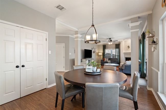 Dining area with a large fireplace, visible vents, ceiling fan, decorative columns, and dark wood-type flooring | Image 16