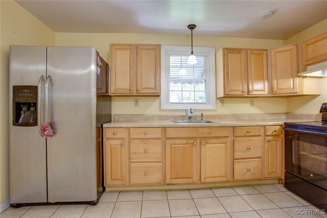 Kitchen with black electric range, sink, stainless steel fridge with ice dispenser, and light tile patterned flooring | Image 18