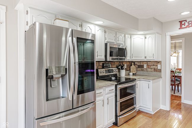 kitchen featuring white cabinets, recessed lighting, light wood finished floors, stainless steel appliances, and decorative backsplash | Image 12