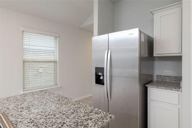Kitchen with stainless steel fridge, vaulted ceiling, light stone countertops, and white cabinetry | Image 10