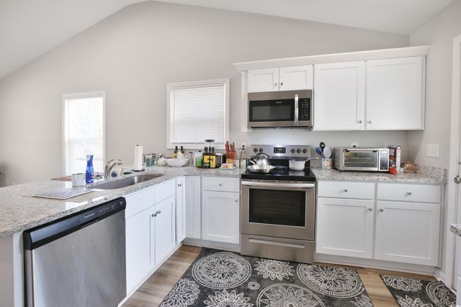 Kitchen with appliances with stainless steel finishes, vaulted ceiling, white cabinets, a peninsula, and light wood-style floors | Image 11