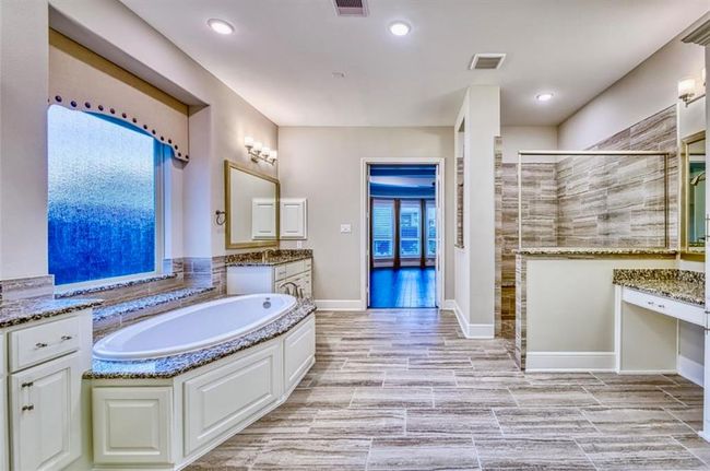 This spacious bathroom features a luxurious soaking tub, dual vanities with granite countertops, and a large walk-in shower. The elegant tile flooring and ample natural light create a serene atmosphere, while the doorway leads to a bright, inviting room. | Image 33