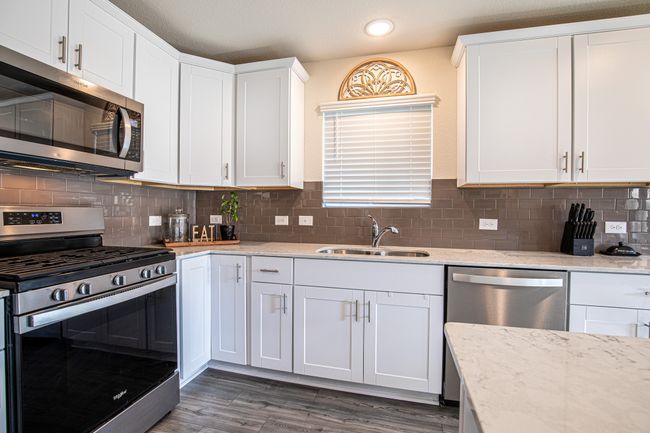 Kitchen featuring appliances with stainless steel finishes, dark wood-style flooring, white cabinets, recessed lighting, and decorative backsplash | Image 7