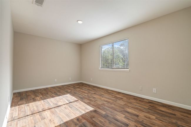 Bright and airy primary bedroom with rich wood-look flooring, soft neutral tones, and peaceful views — a perfect place to unwind in South Austin comfort. | Image 12