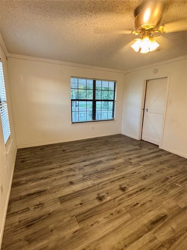 Empty room featuring dark wood-style flooring, a textured ceiling, ornamental molding, and ceiling fan | Image 17