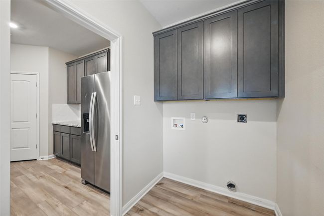 Laundry room featuring light wood-style flooring, hookup for an electric dryer, hookup for a gas dryer, baseboards, and cabinet space | Image 17