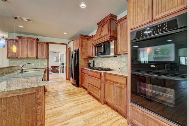 Kitchen with light wood finished floors, a sink, visible vents, light stone counters, and black appliances | Image 13