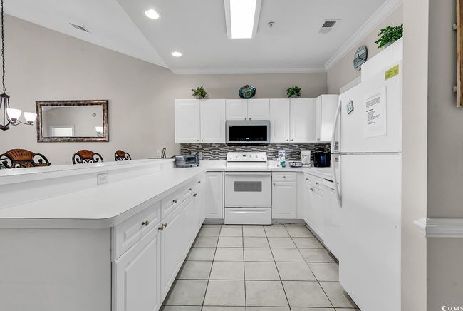 Kitchen featuring white appliances, a peninsula, backsplash, light tile patterned flooring, and visible vents | Image 4