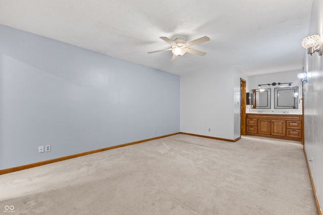 unfurnished bedroom with light colored carpet, baseboards, connected bathroom, and a ceiling fan | Image 26