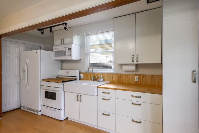 Kitchen with white appliances, a sink, white cabinets, light wood finished floors, and butcher block counters | Image 26