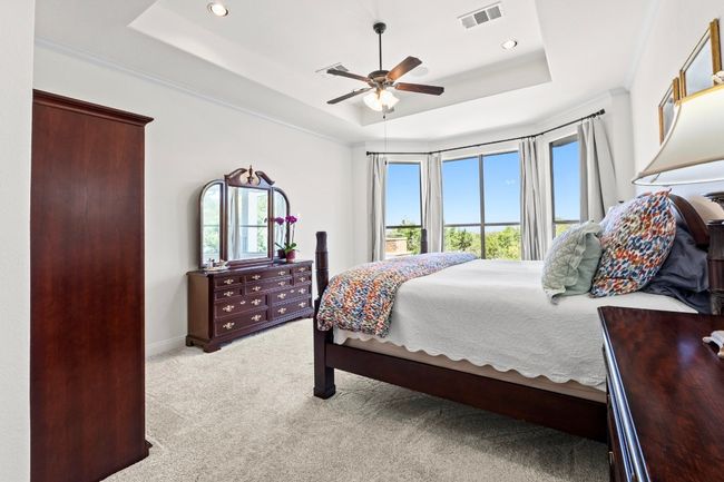 The opulent primary bedroom suite offers tray ceilings, crown molding, bay window seating area and spectacular walk-in closet. | Image 13