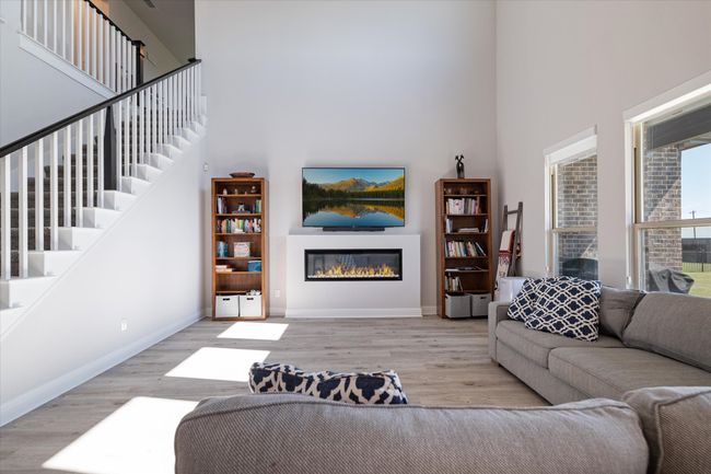 Living room with a towering ceiling, wood finished floors, baseboards, a glass covered fireplace, and stairs | Image 15