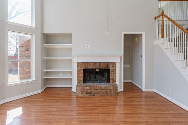 Unfurnished living room featuring baseboards, stairway, wood finished floors, a brick fireplace, and built in shelves | Image 5