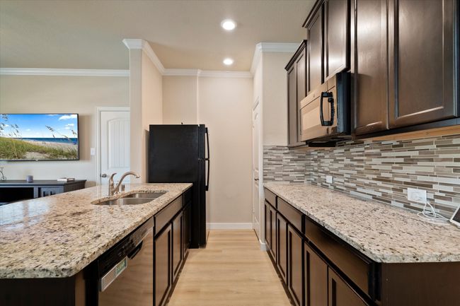 Kitchen featuring black appliances, a sink, crown molding, dark brown cabinetry, and decorative backsplash | Image 31
