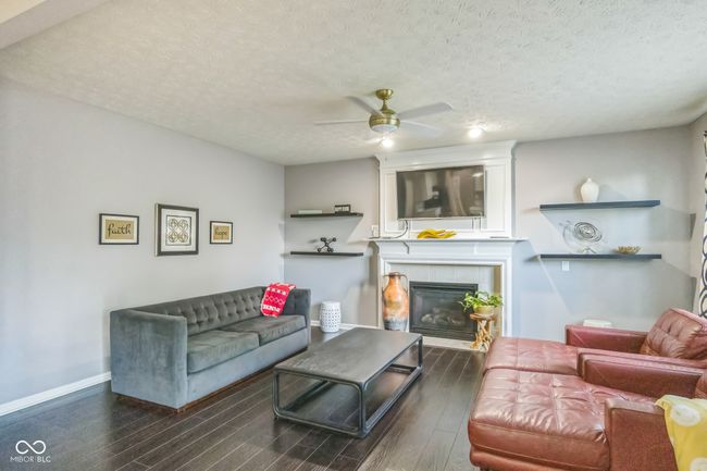 living area featuring a ceiling fan, wood finished floors, a tile fireplace, and a textured ceiling | Image 4