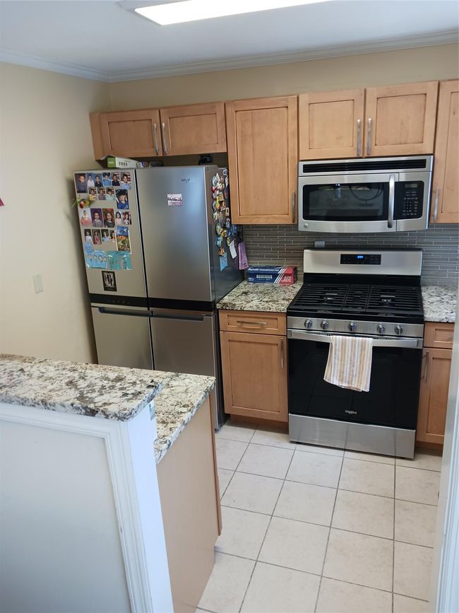Kitchen featuring stove, freestanding refrigerator, decorative backsplash, stainless steel microwave, and crown molding | Image 13