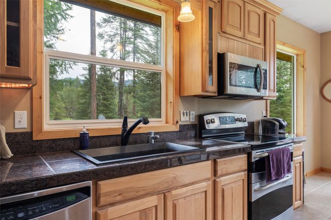 Kitchen with appliances with stainless steel finishes, glass insert cabinets, light tile patterned floors, and tile counters | Image 38