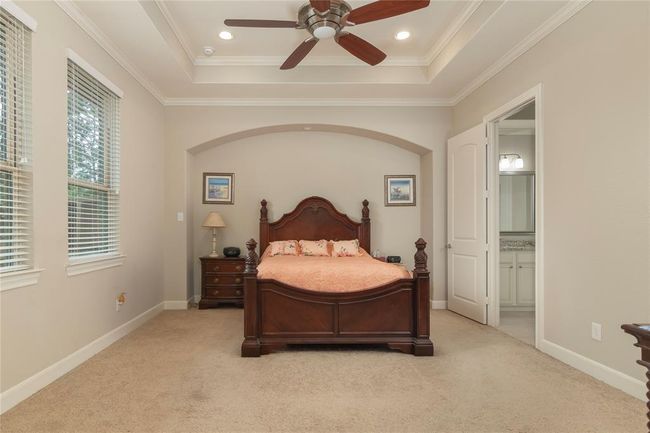 This primary bedroom features a cozy atmosphere and privacy. Perfect place to end your day and unwind. It has soft carpet flooring, a ceiling fan, and ample natural light from the windows. The room connects to an en-suite bathroom, offering convenience and privacy. | Image 26
