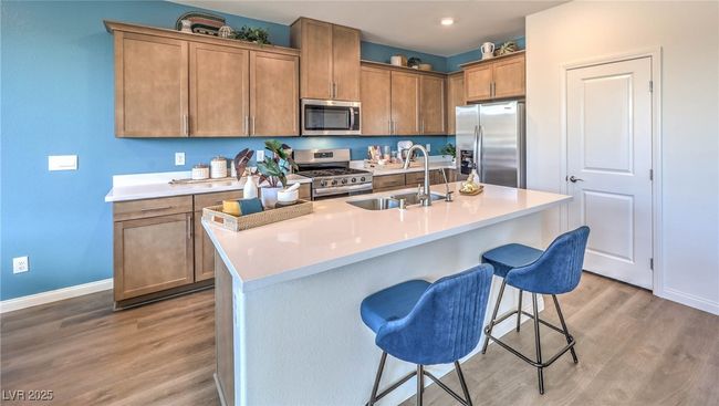 Photo is representational only; actual home finishes may vary. Kitchen with appliances with stainless steel finishes, a sink, baseboards, light wood-type flooring, and a kitchen bar | Image 4
