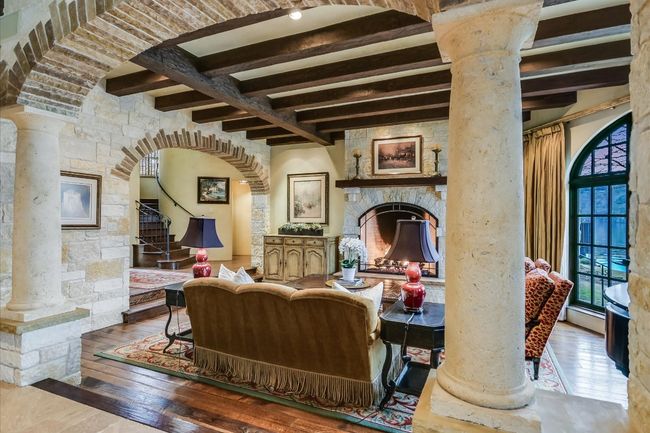 Living area with wood-type flooring, a stone fireplace, beamed ceiling, and ornate columns | Image 10