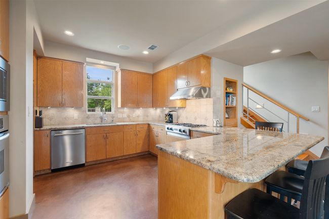 Kitchen with dishwasher, a peninsula, stove, concrete flooring, and a sink | Image 16